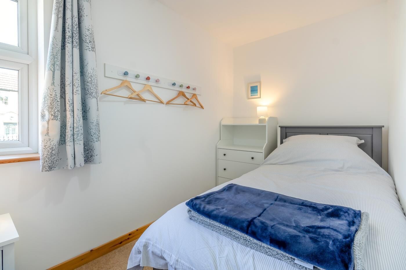 Una camera da letto con un letto, un comodino, una lampada a sospensione e una finestra con tende.