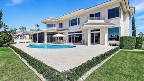 Une maison moderne à deux étages, dotée d’une piscine, d’un patio couvert et d’une pelouse bien entretenue.