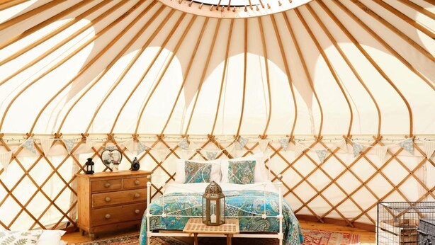 L’intérieur chaleureux d’une yourte, avec un lit, une commode en bois et des tapis.