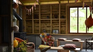 L’intérieur d’un chalet rustique, avec une cheminée, des meubles en osier et une vue sur l’extérieur.