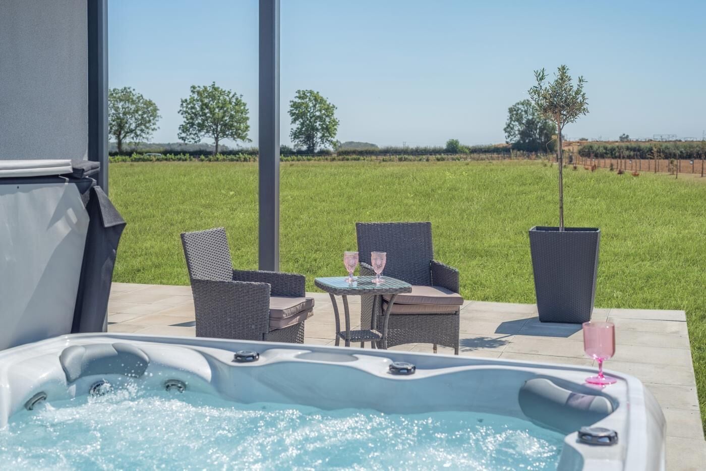 Ein Whirlpool mit zwei Stühlen und einem Tisch, umgeben von einer Wiese und Bäumen.
