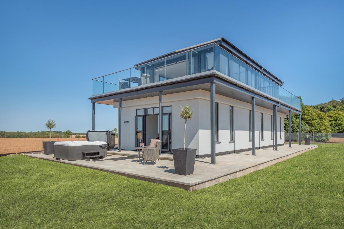 Een modern huis met een glazen conservatorium, buitenmeubelen en een plat dak.