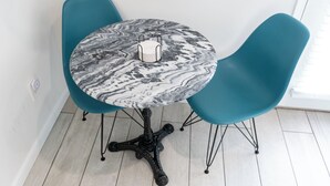 Et rundt bord med marmorlook, to teal farvede stole og en sort metalfod.