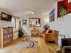 Ein Wohnzimmer mit Fernseher, Bücherregal, Esstisch, Sofa und einem Spiegel.