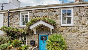 A stone building with a blue door, a small porch with plants, and a potted plant in front. - 2 Bed in Y Felinheli (oc-40860) (Y Felinheli)