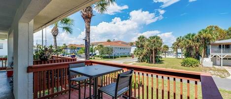 A covered outdoor deck with a table and chairs, overlooking a residential area with palm trees and houses.