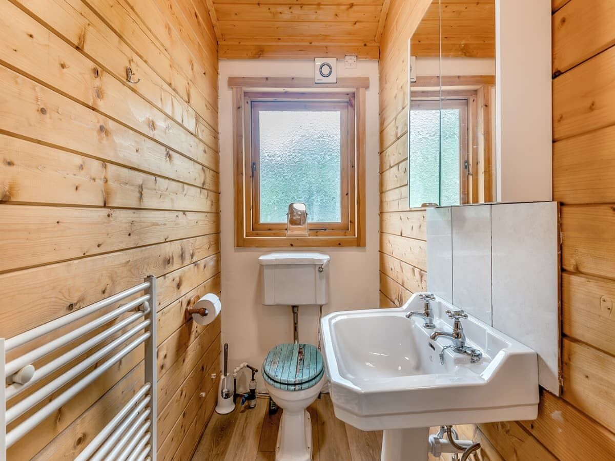 Une petite salle de bain en bois, avec des dimensions réduites, comprenant des toilettes, un lavabo et une fenêtre.