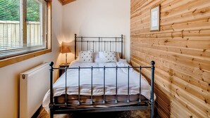 Een slaapkamer met een houten plafond, een metalen bedframe, wit beddengoed, een bedlamp en een raam met zonwering.