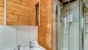 Een houten badkamer met een douchecabine van glas, een witte wastafel en een spiegel.