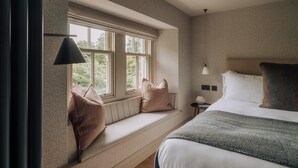 Ein Schlafzimmer mit großem Fenster, einem Bett, einem Nachttisch und einer Lampe.
