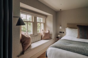 Ein Schlafzimmer mit großem Fenster, einem Bett, einem Nachttisch und einer Lampe.