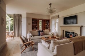 Ein Wohnzimmer mit Sofa, Sesseln, Couchtisch, Kamin und Fernseher.