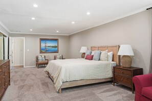 Ein Schlafzimmer mit einem großen Bett, zwei Nachttischen mit Lampen, einer Kommode, einem Sessel und einem Gemälde an der Wand.