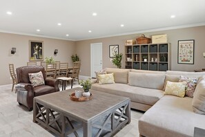 Un salon comprenant un fauteuil en cuir marron, une table basse en bois, un canapé beige et un coin repas avec des chaises et une table en bois.