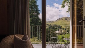 A room with a large sliding glass door leading to an outdoor patio with a table and chairs, a view of hills, and a chair with a cushion. - 2 Bed in Grasmere (oc-lr246) (Penrith)