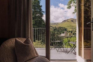 A room with a large sliding glass door leading to an outdoor patio with a table and chairs, a view of hills, and a chair with a cushion. - 2 Bed in Grasmere (oc-lr246) (Penrith)