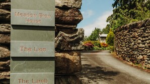 A stone wall with signs indicating 'Meadow Brow House', 'The Lion', and 'The Lamb'. - 2 Bed in Grasmere (oc-lr246) (Penrith)