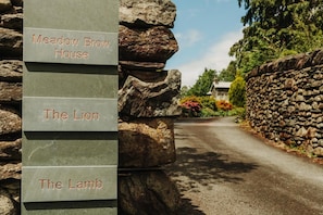 A stone wall with signs indicating 'Meadow Brow House', 'The Lion', and 'The Lamb'. - 2 Bed in Grasmere (oc-lr246) (Penrith)