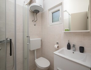 Ein Badezimmer mit Duschkabine, Toilette, Waschbecken mit Spiegel und Pflegeprodukten.