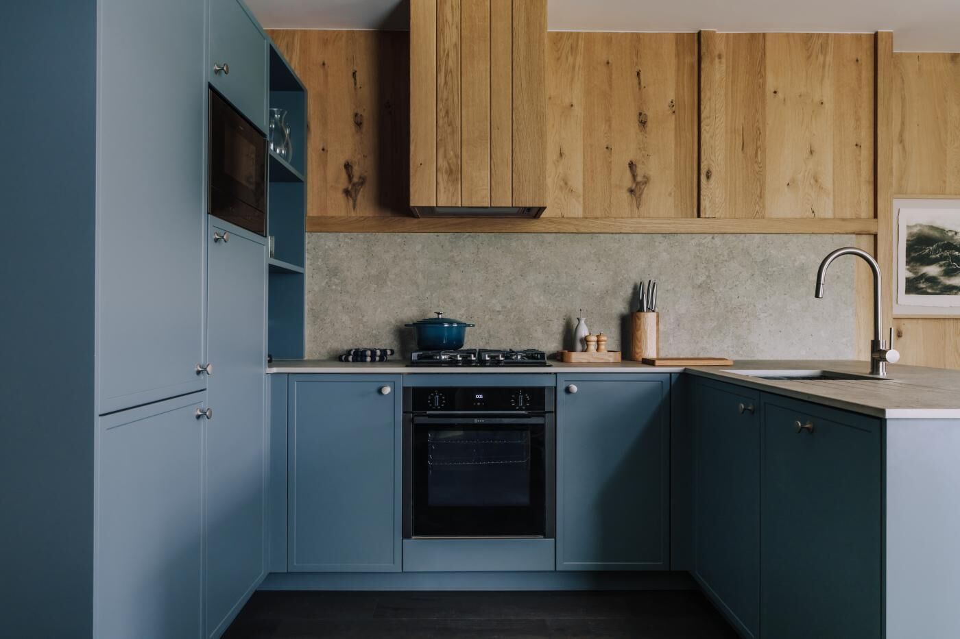 Eine Küche mit blauen Schränken, einem Herd, einem Backofen, einer Spüle und Holzschränken oben.