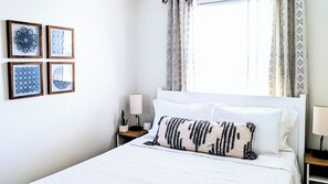 Ein ordentlich bezogenes Bett mit weißen Leinen, einer Nachttischlampe und einem Nachttisch mit einer Pflanze.