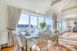 A dining area with a table set for four, large windows, and a view of the sea. - 5 Bed in Rock (oc-u22448) (Rock)