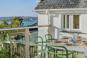 A balcony with a view of a coastal cityscape, a table with chairs, and a window with curtains. - 5 Bed in Rock (oc-u22448) (Rock)