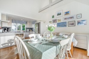 Eine moderne Küche mit weißen Schränken, ein Essbereich mit grüner Tischdecke und Blick ins Freie.