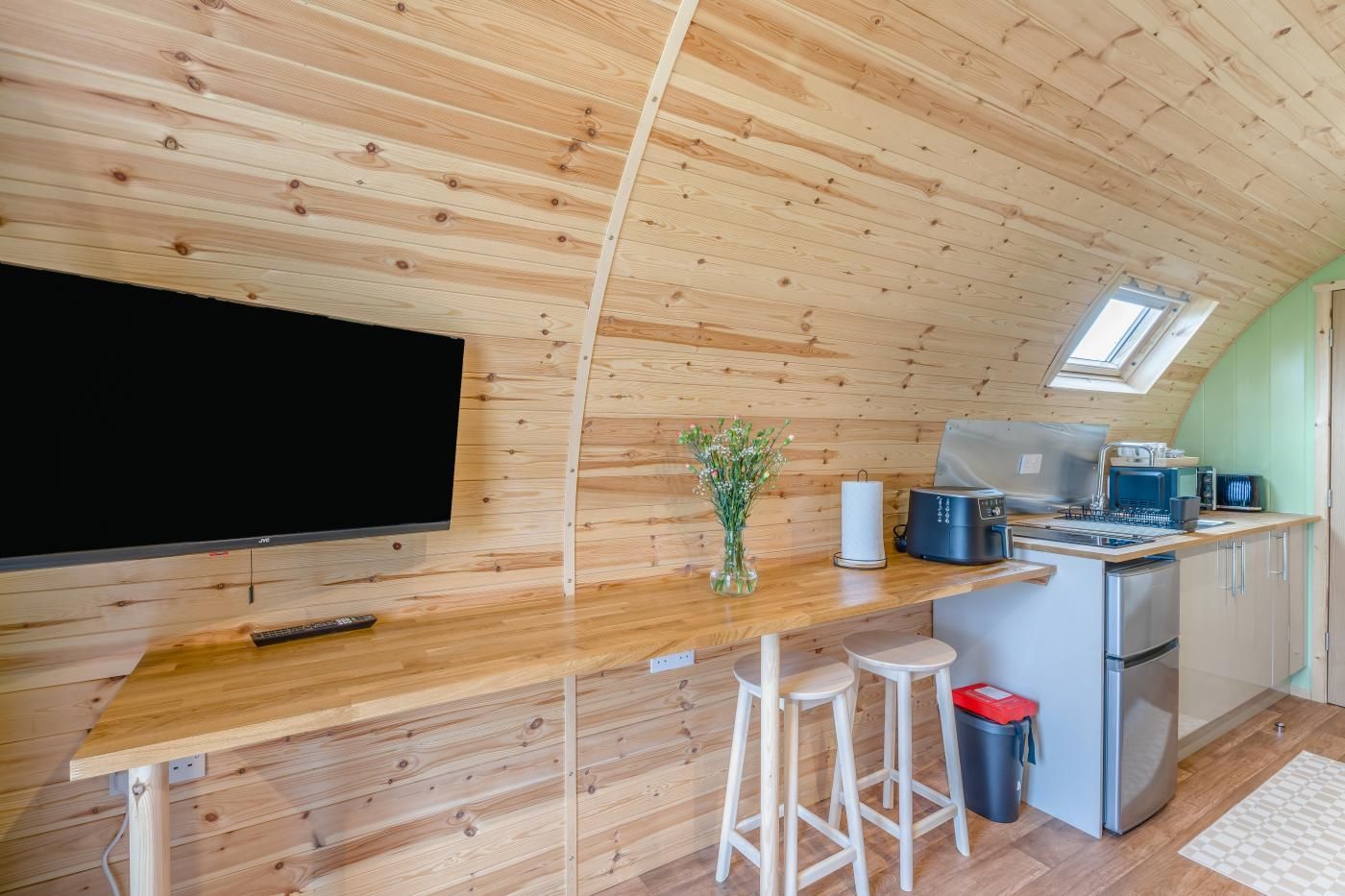 Een compacte keuken met houten wanden, een flatscreen televisie, een klein eiland met krukken en een koelkast.