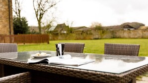 Un área de comedor al aire libre con sillas de mimbre, una mesa de vidrio, un plato de comida y una revista sobre la mesa.
