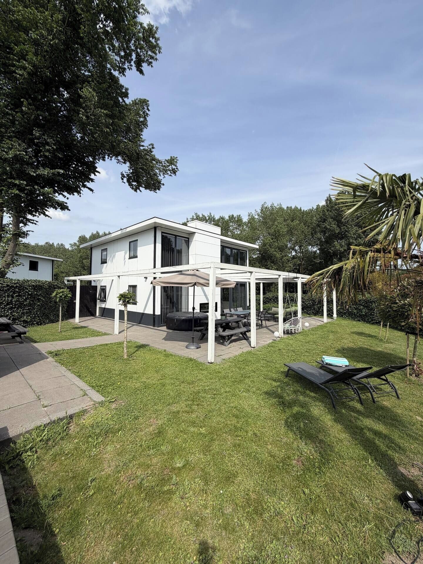 A modern two-story house with a covered patio area, a lawn, and outdoor furniture.