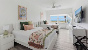 A hotel room with a bed, a desk, a TV, and a window with a view of the beach. - Be A Nomad | 2BR Beach Apartment | 1-Min Walk to Sand | Sleeps 4 (Jacksonville Beach)
