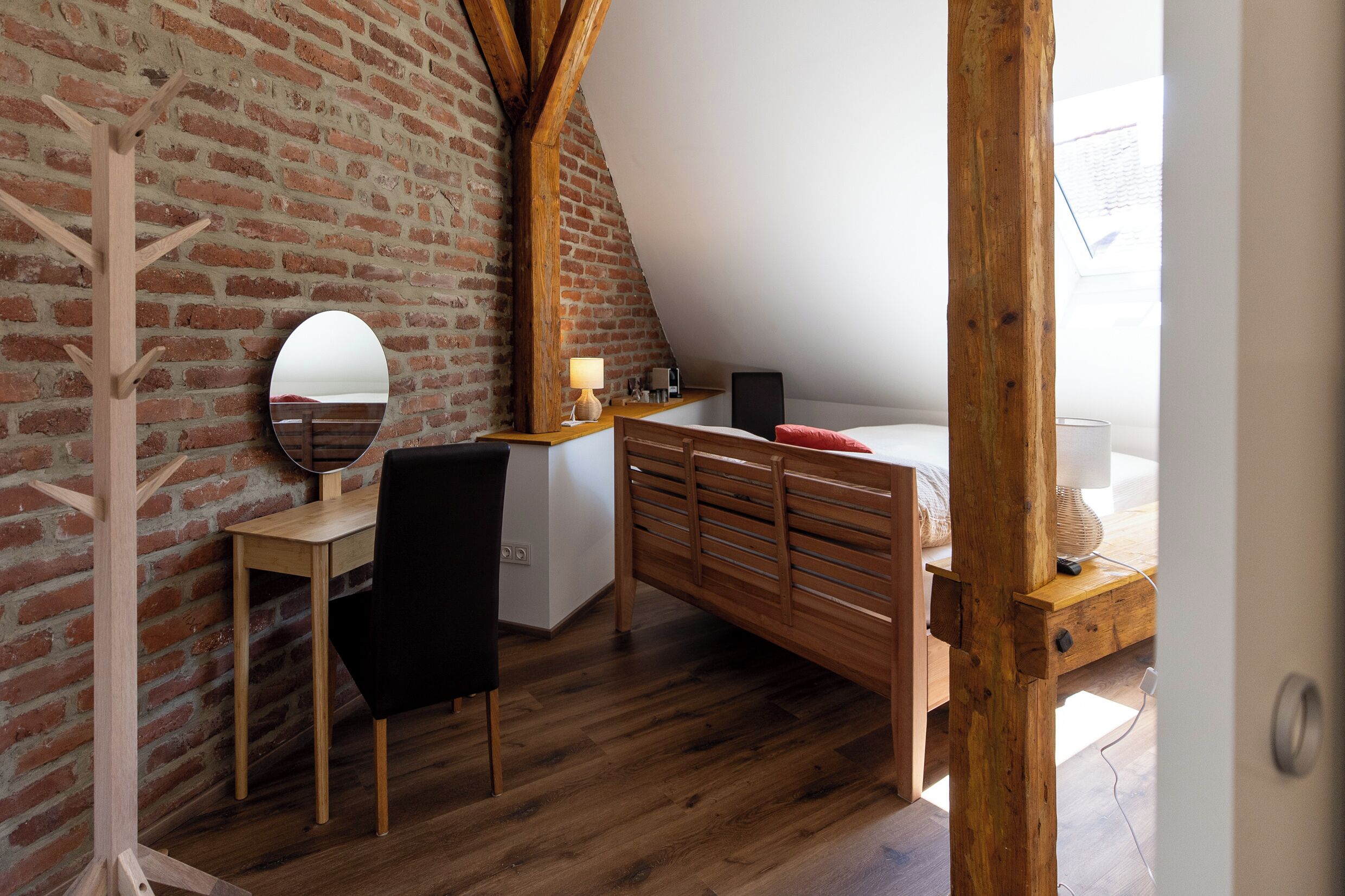 Een slaapkamer met een schuine plafond, een houten bureau, een stoel, een bed en een spiegel.