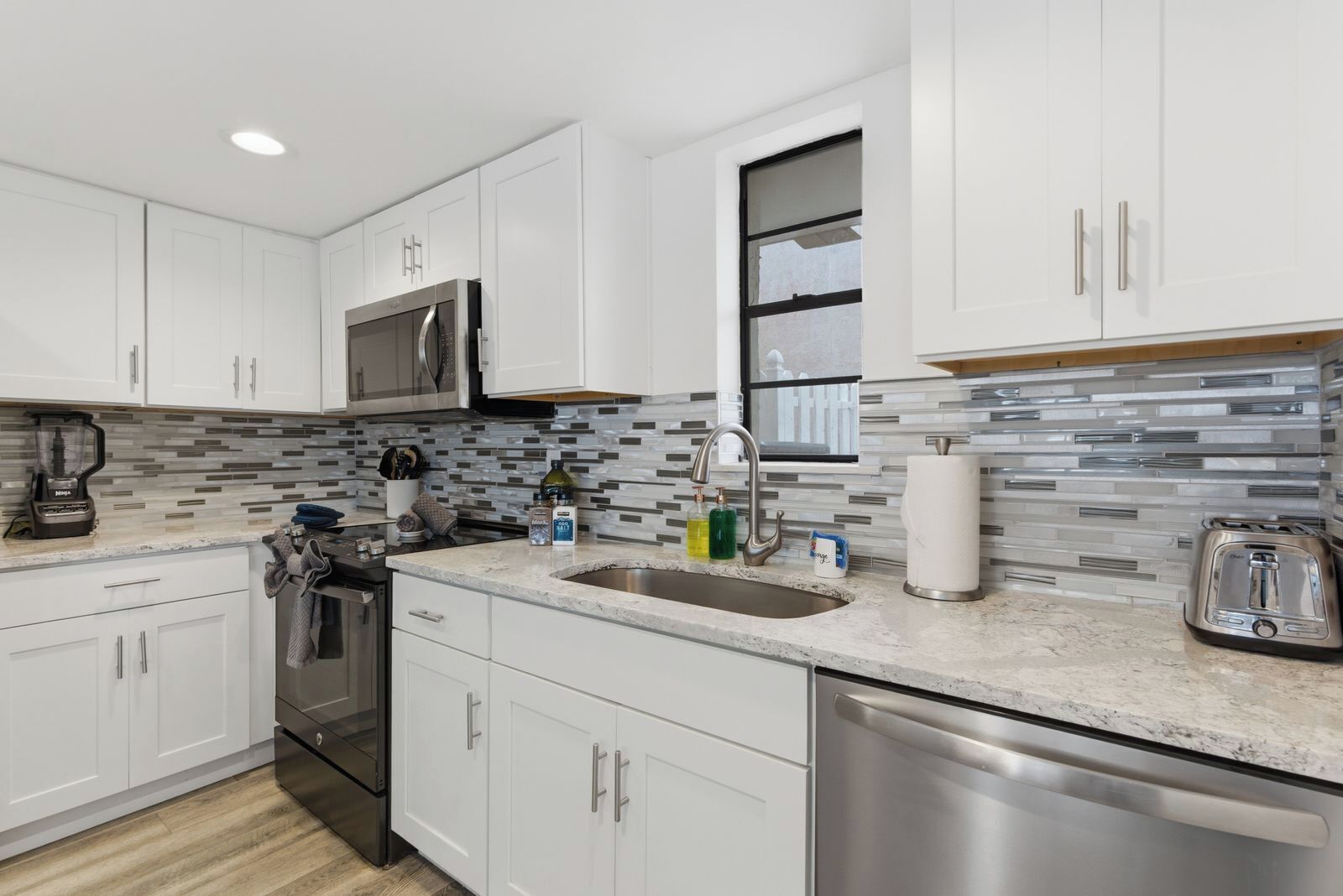 A modern kitchen with white cabinets, a stainless steel dishwasher, a microwave, and a toaster.