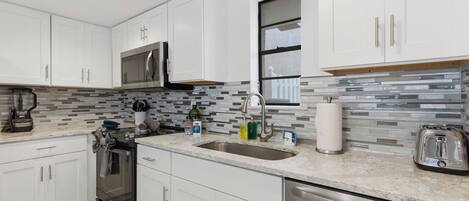 A modern kitchen with white cabinets, a stainless steel dishwasher, a microwave, and a toaster.