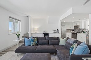 Ein modernes Wohnzimmer mit einem Ecksofa, einem kleinen Tisch und einer Küche im Hintergrund.