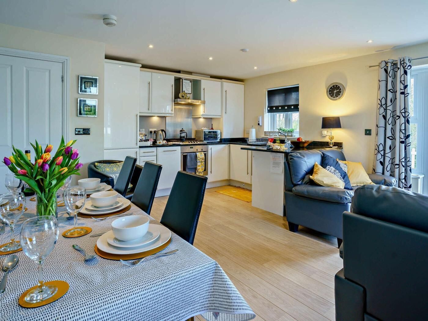 Een moderne keuken met witte kastjes, een eethoek met een tafel voor twee personen, en een zithoek met een bank.