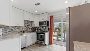 A modern kitchen with white cabinets, a microwave, an oven, and a wooden floor. - Be A Nomad | 3 Bed 3 Bath | 1 Min to Jacksonville Beach | Sleeps 6 (Jacksonville Beach)