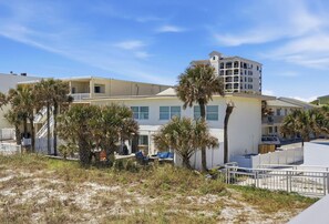 Un hôtel situé sur la côte, composé de plusieurs bâtiments, bordé de palmiers et donnant sur une plage de sable.