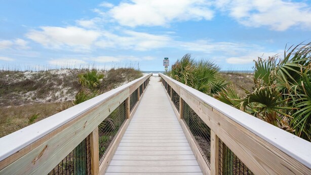 Une promenade en bois menant à la plage, avec un ciel dégagé.