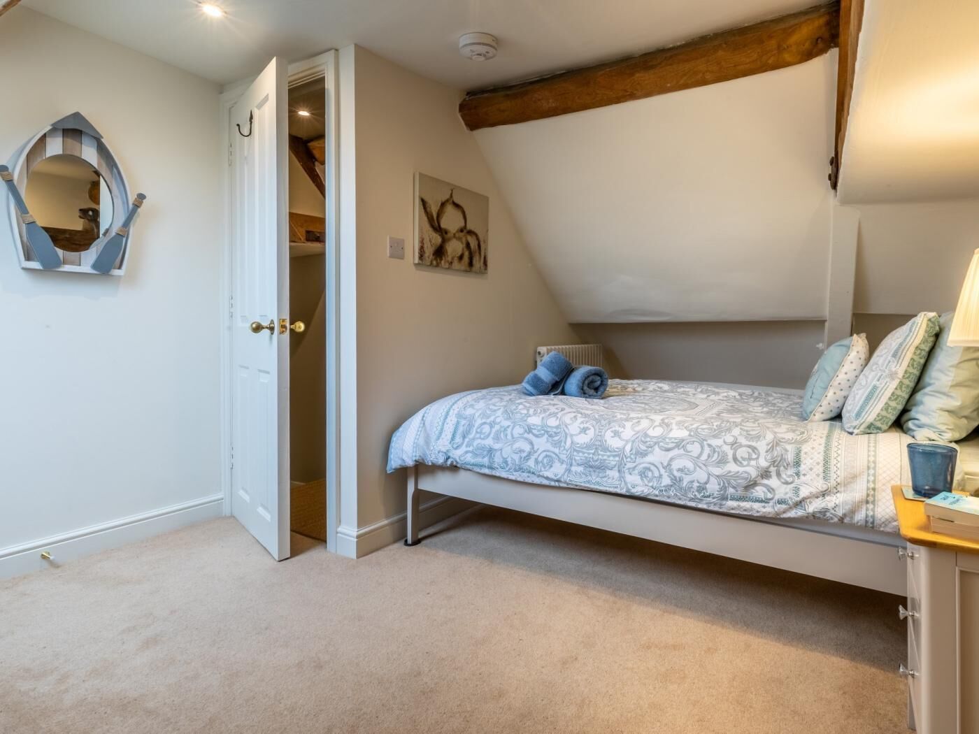 Een slaapkamer met een bed, een deur naar een trap, een spiegel en een kunstwerk aan de muur.
