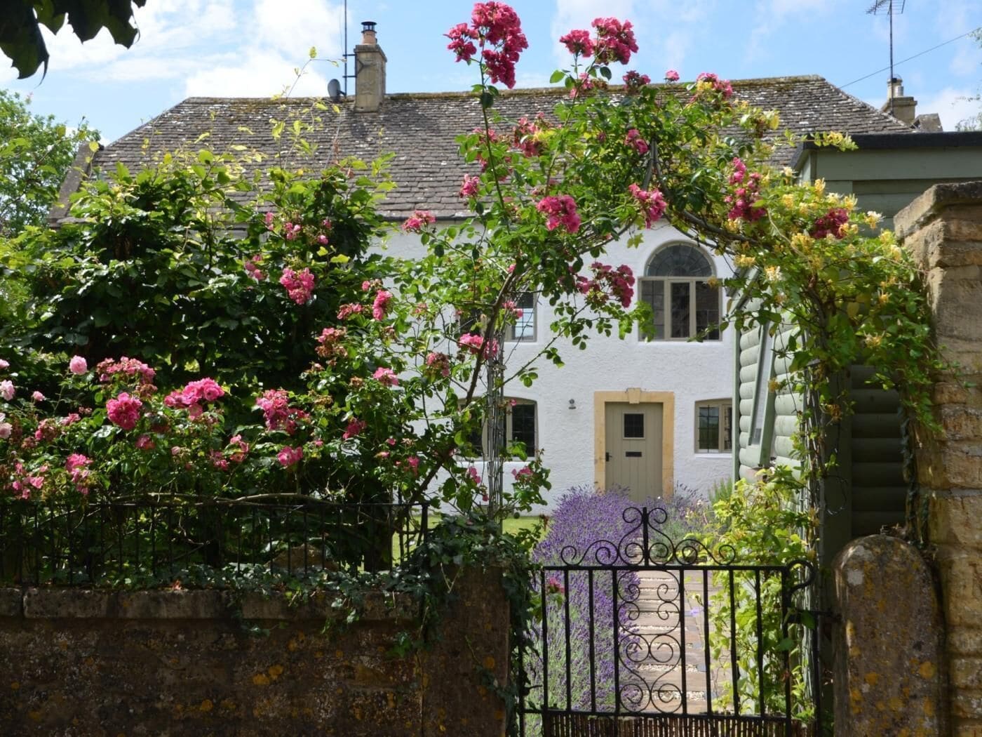 A white building with a grey roof, a gated entrance, and pink flowering plants.