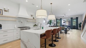 A modern kitchen with a marble island, pendant lights, and bar stools. - Be A Nomad | Oceanview | Golf Simulator- Sleeps 10 (Jacksonville Beach)