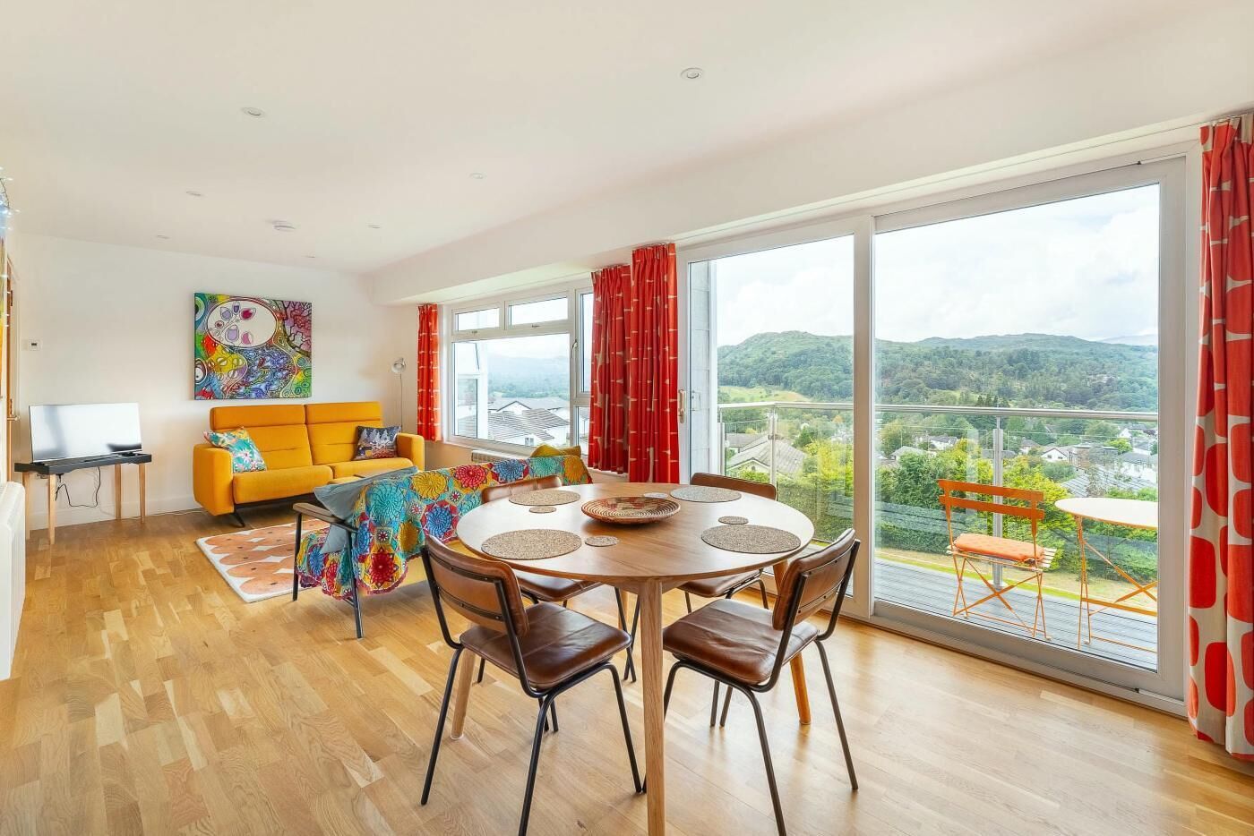 A modern living room with a dining area, large windows, and a view of the countryside.