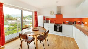 A modern kitchen with a dining area, large windows, and a view of the city. - 2 Bed in Ambleside (oc-lr111) (Ambleside)