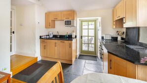 A compact kitchen with wooden cabinets, a black countertop, a microwave, and a door leading to an outdoor area. - 1 Bed in Troutbeck (oc-lr027) (Troutbeck)