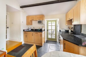 A compact kitchen with wooden cabinets, a black countertop, a microwave, and a door leading to an outdoor area. - 1 Bed in Troutbeck (oc-lr027) (Troutbeck)
