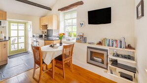 A kitchen with wooden cabinets, a dining table with chairs, a TV mounted on the wall, and a fireplace. - 1 Bed in Troutbeck (oc-lr027) (Troutbeck)