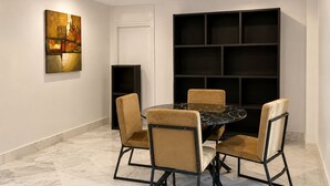A dining area with a round table, four chairs, a painting on the wall, and a black shelving unit. - Luxury Apartment in Ain Zaghouan (Ain Zaghouan)