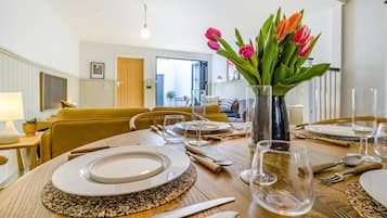 A dining area with a round table set for four, a vase with tulips, and a view into the adjacent living room.